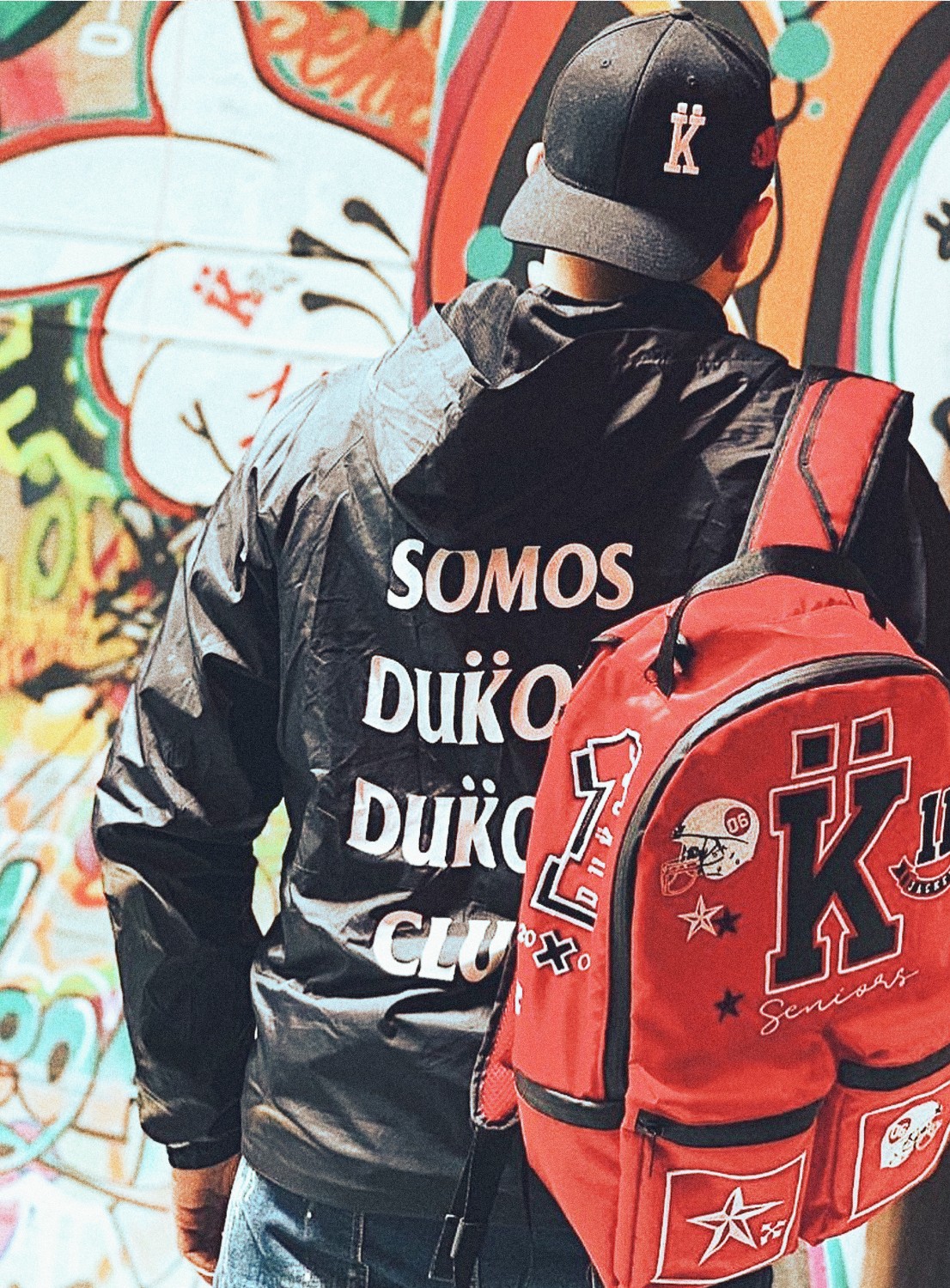 Hombre joven de espaldas, usando chaqueta, gorra y morral personalizado de DUKOPP
